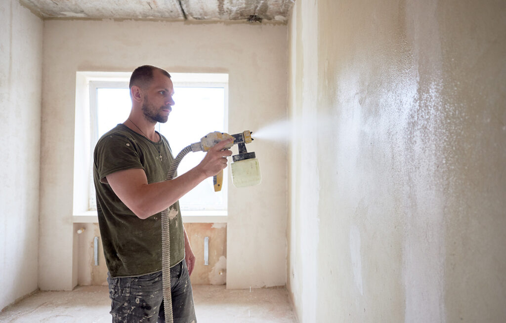 Man painting with airbrush apartment repairment against small window in the daytime
